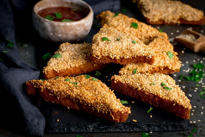 Sesame prawn toast with sweet chilli sauce on a dark serving board
