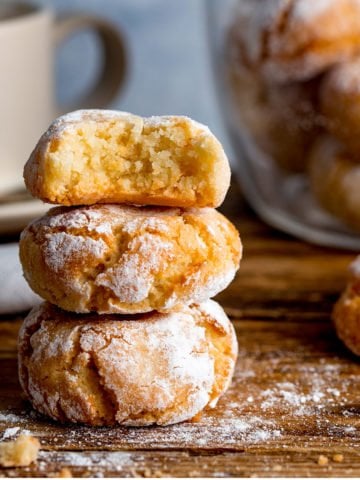 Italian Amaretti cookies in a pile on a wooden board with a cup in the background.