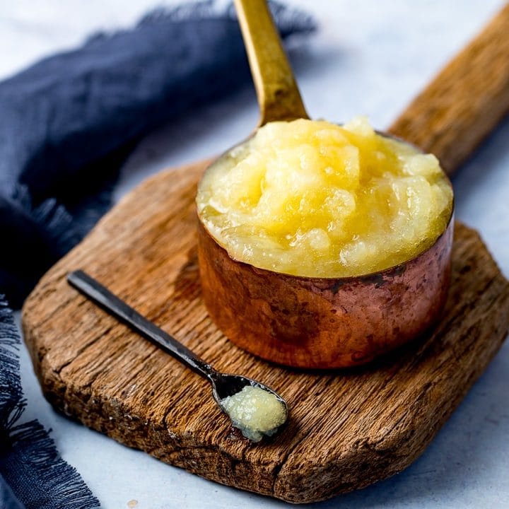 Apple sauce in a copper pan on a wooden board against a light background