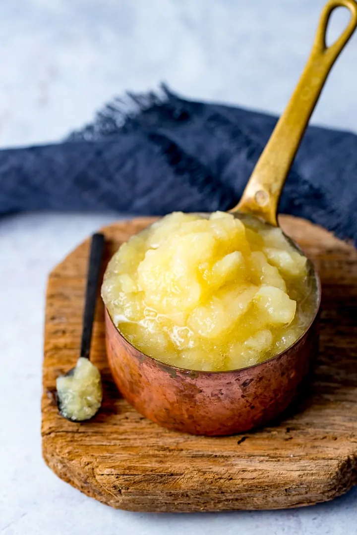 Apple sauce in a copper pan on a wooden board with a spoonful taken out