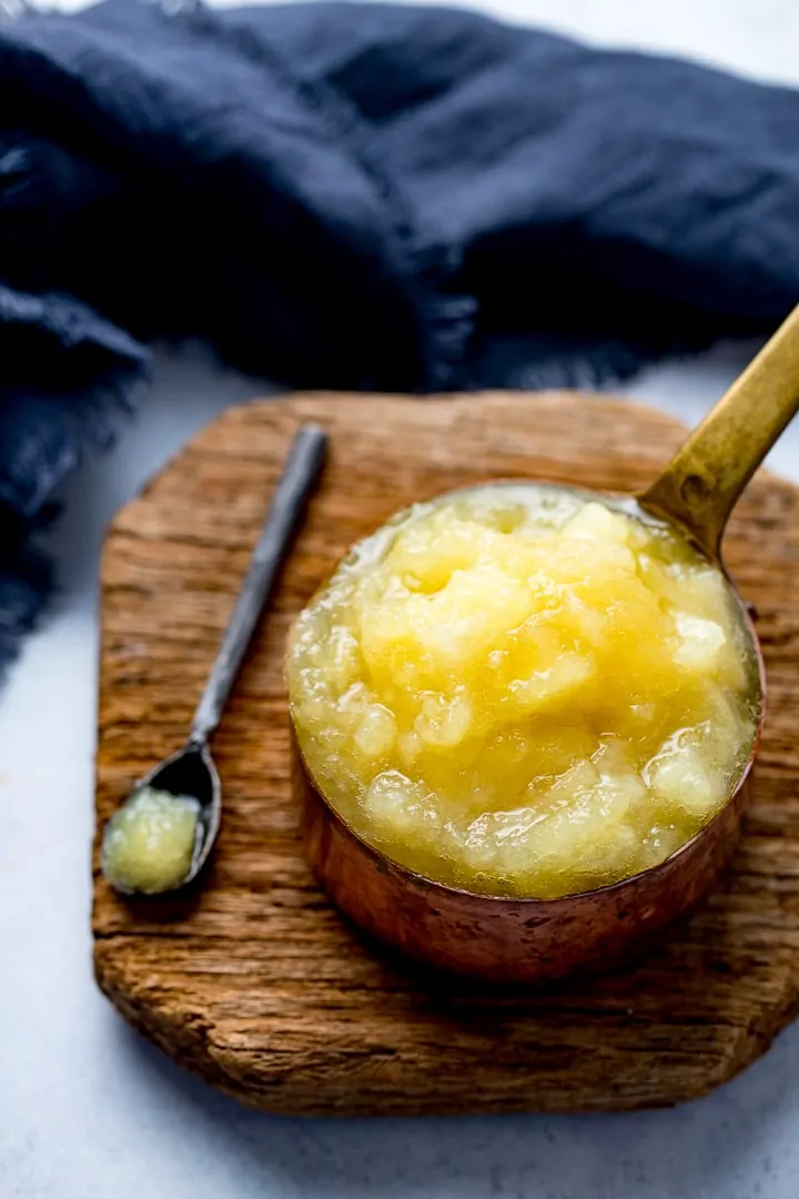 Apple sauce in a copper pan on a wooden board next to a blue teatowel