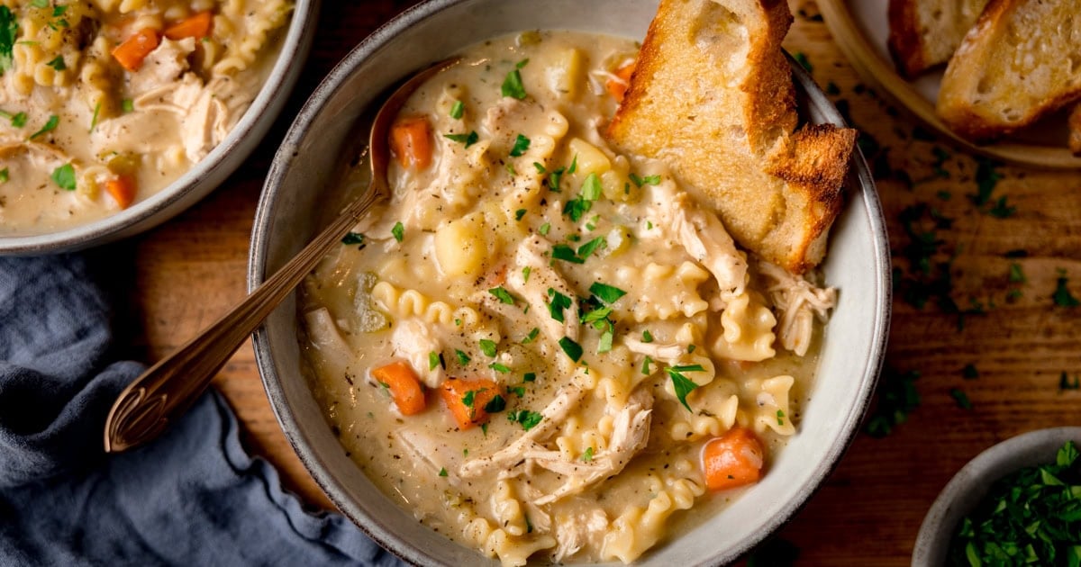 A bowl of creamy chicken soup with diced carrots, potatoes and pieces of flat pasta.