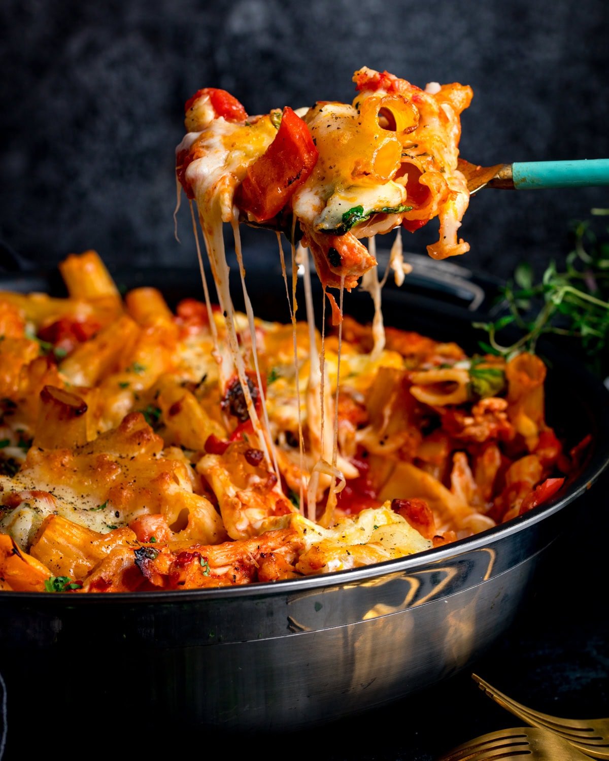 A fork lifts a portion of cheesy Turkey Pasta Bake from a pan, gooey melted cheese stretching with the lift.