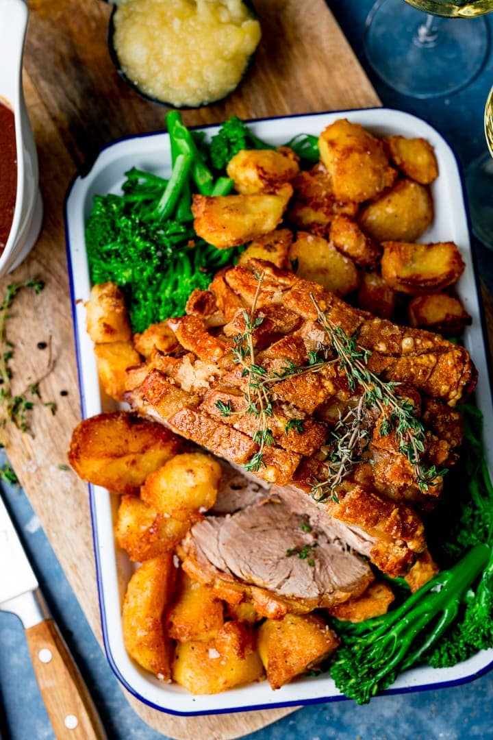 Overhead of roast pork with crispy crackling on a tray with roast potatoes, broccoli, apple sauce and gravy