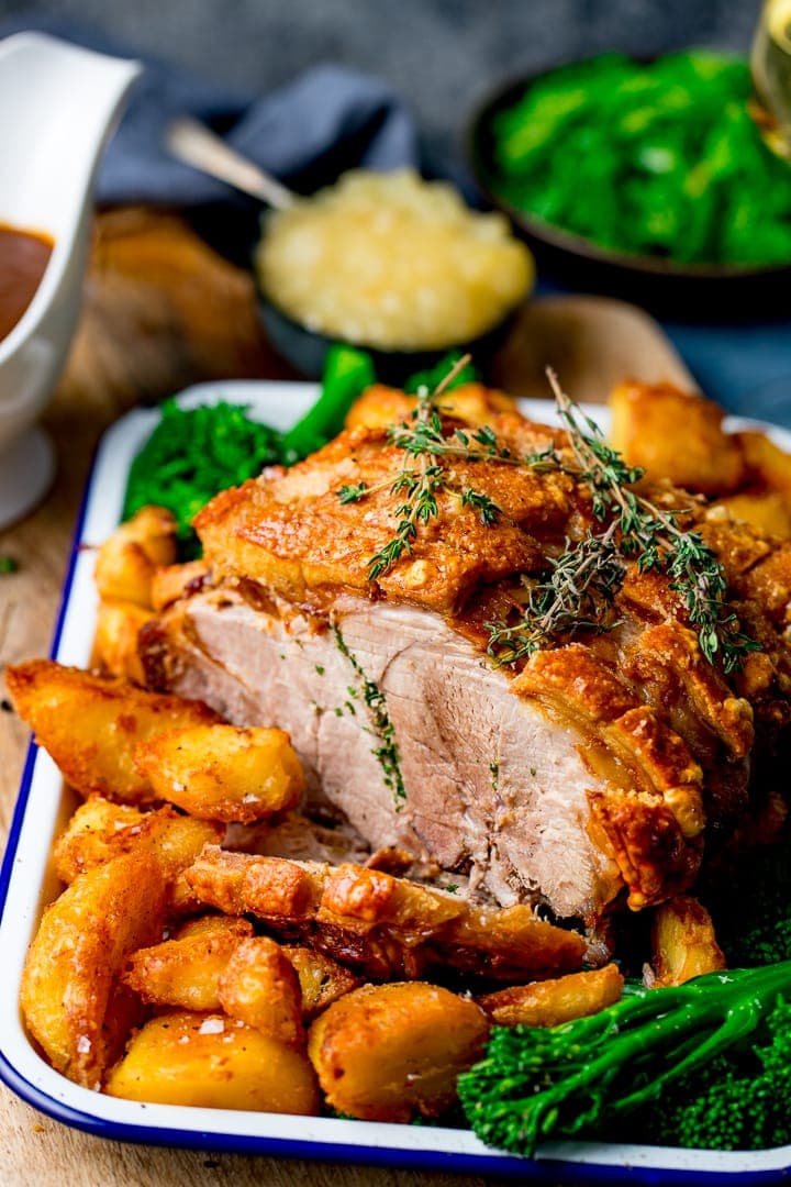Joint of roast pork in a tray with roast potatoes and apple sauce