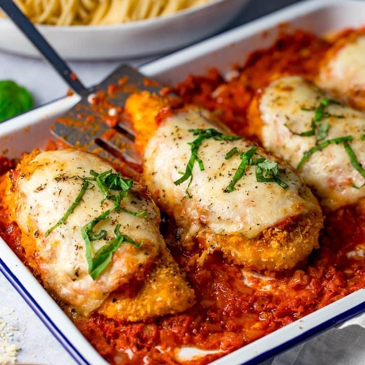 White baking tray with chicken parmesan with one piece of chicken being taken