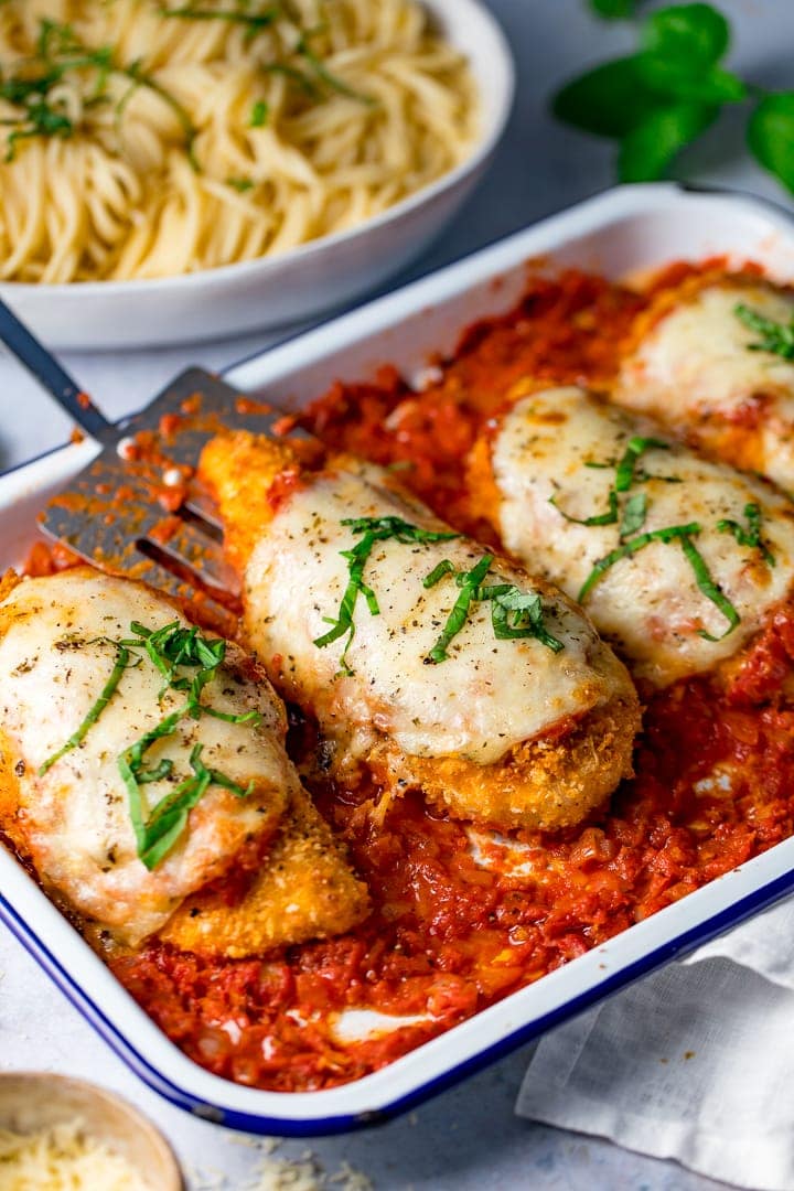 Tray of chicken parmesan with one piece of chicken being taken