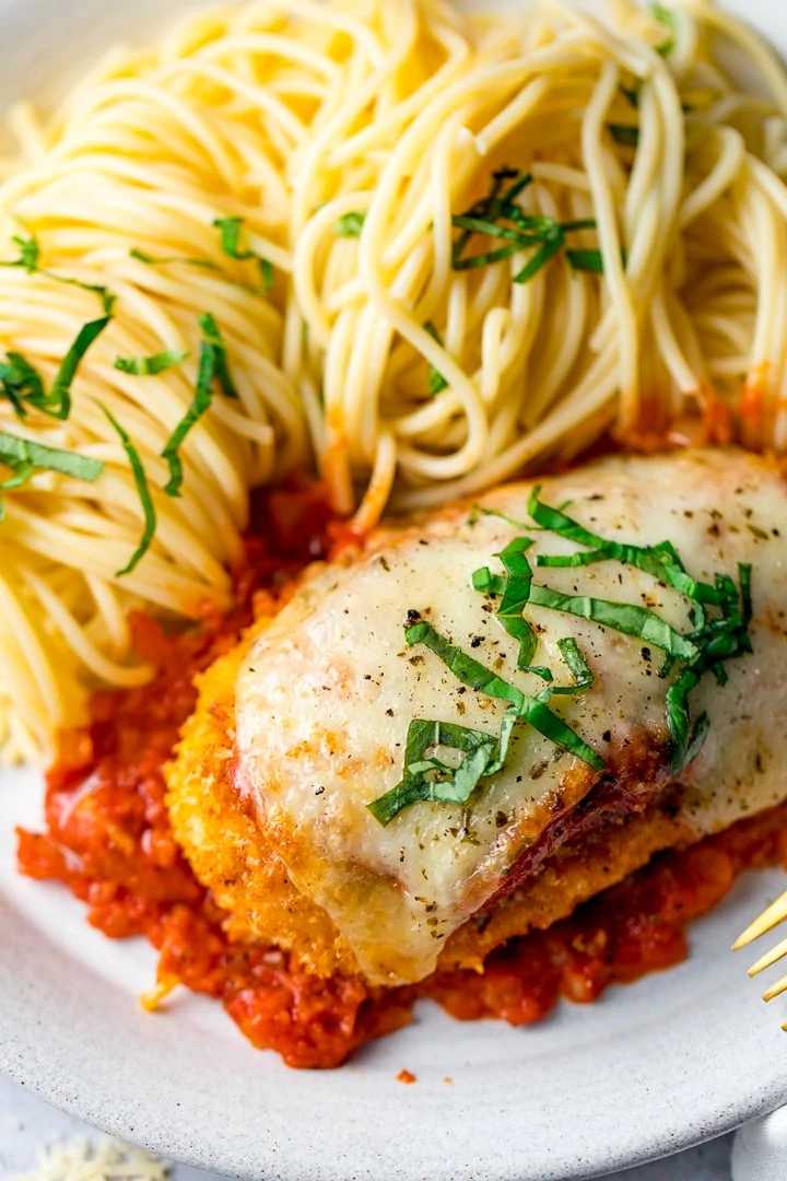 Chicken parmesan on a white plate with spaghetti