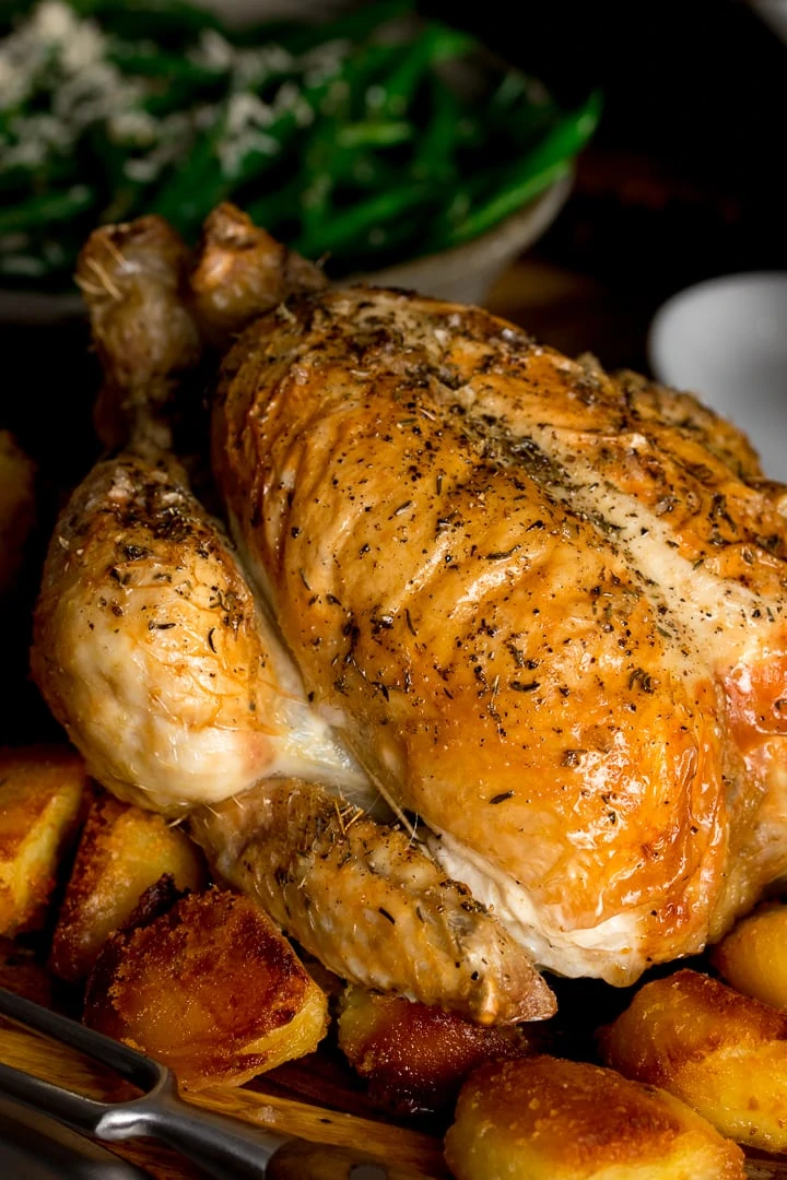 Close up of roast chicken on a board with potatoes