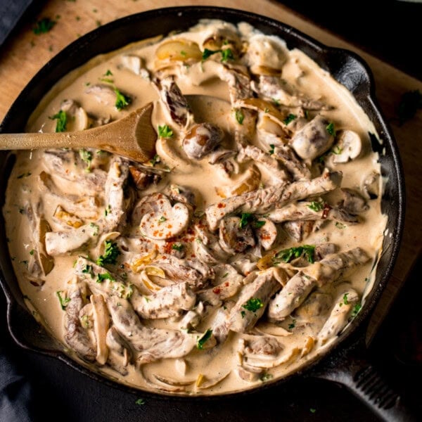 A frying pan filled with creamy Beef Stroganoff, featuring sliced beef, mushrooms, onions, and a rich sauce, garnished with chopped parsley.