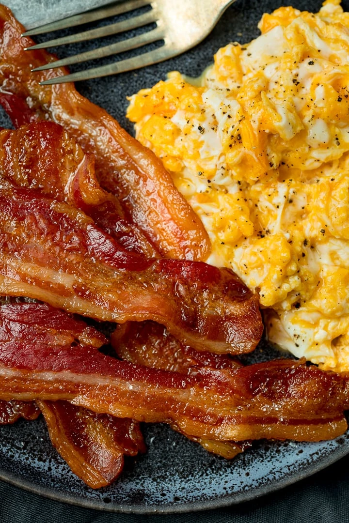 Close up image of bacon and scrambled eggs on a dark plate