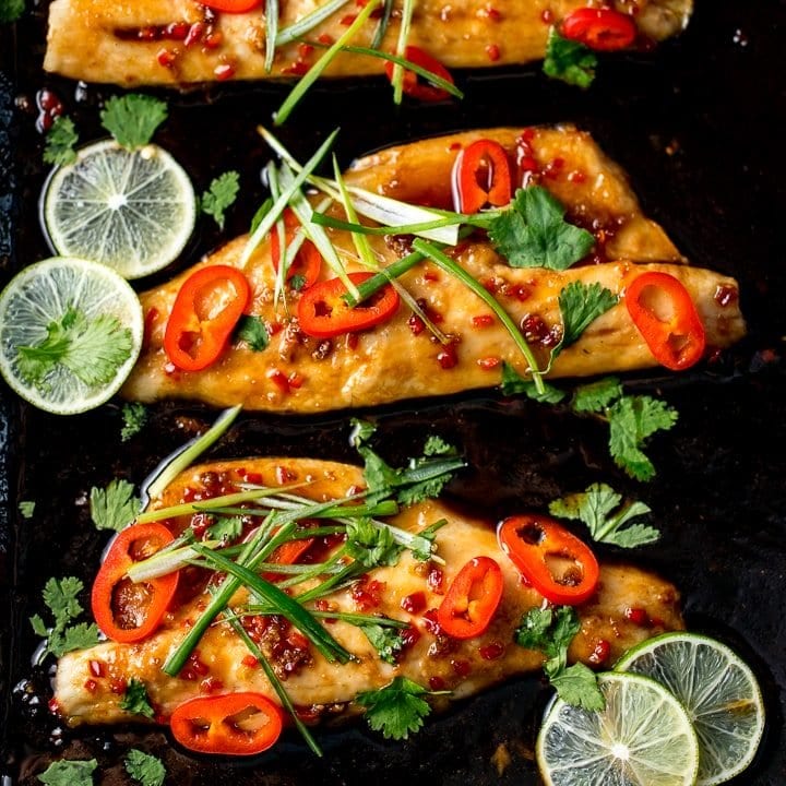 Asian-style sea bass fillets on a baking tray with spring onions and chillies