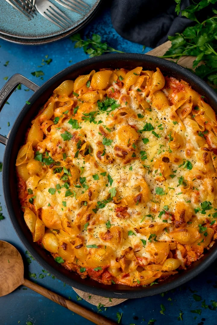 Overhead of tuna tomato pasta bake in a dark pan on a blue background