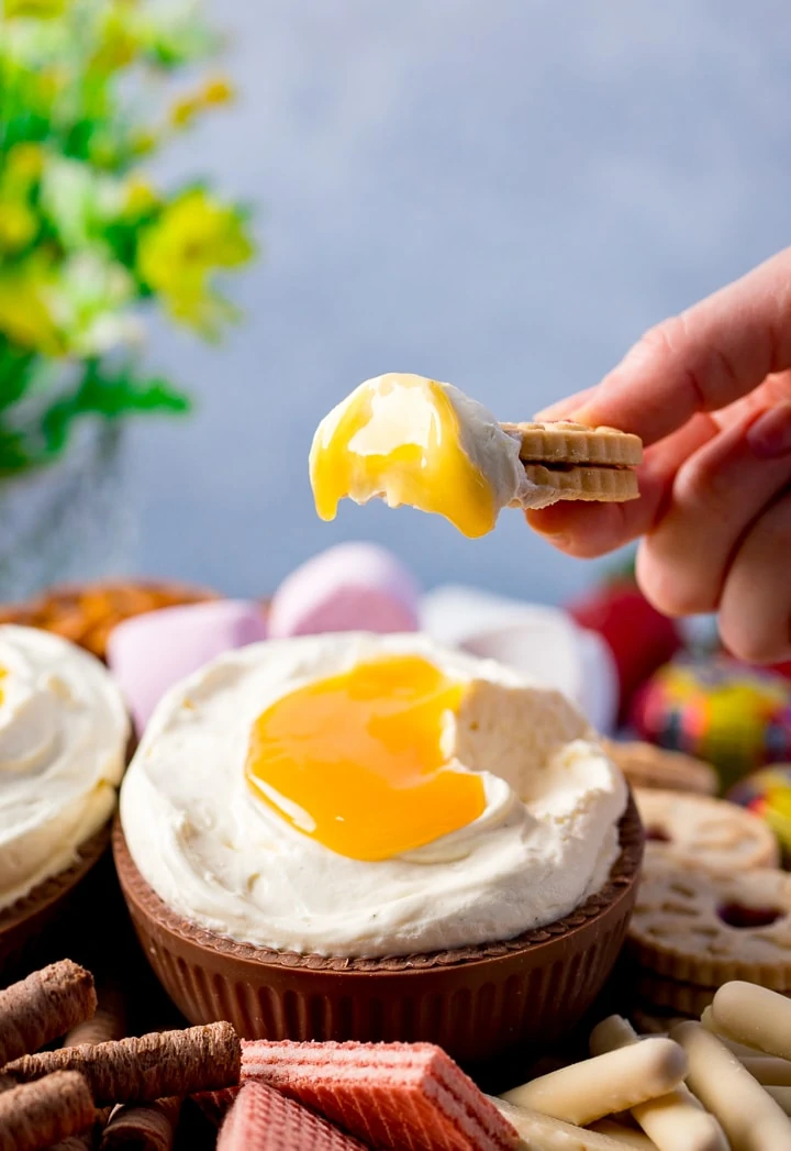 Biscuit being dipped into a giant creme egg cheesecake dip