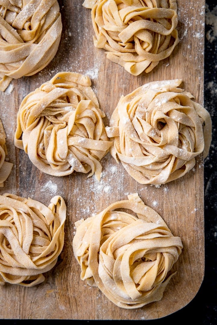 Piles of homemade pasta with flour sprinkled on, on wooden board