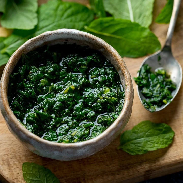 Square image of mint sauce in a small dish on a wooden board