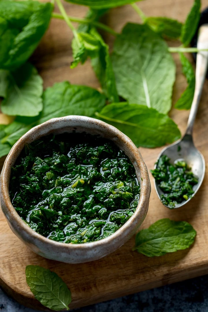 Mint sauce in a small dish on a wooden board with a spoon next to it