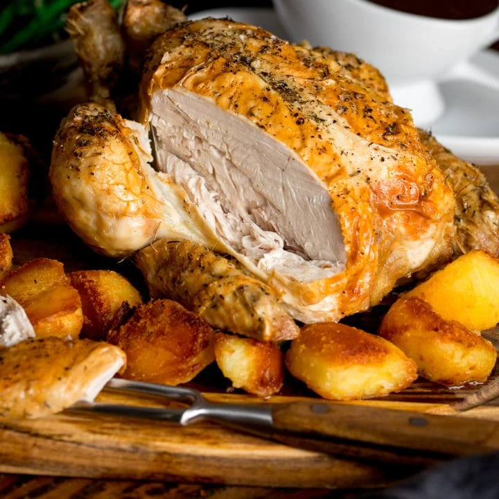 Sliced roast chicken on a board with potatoes and gravy.