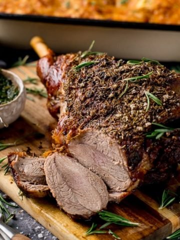 Sliced roast leg of lamb on a board with mint sauce