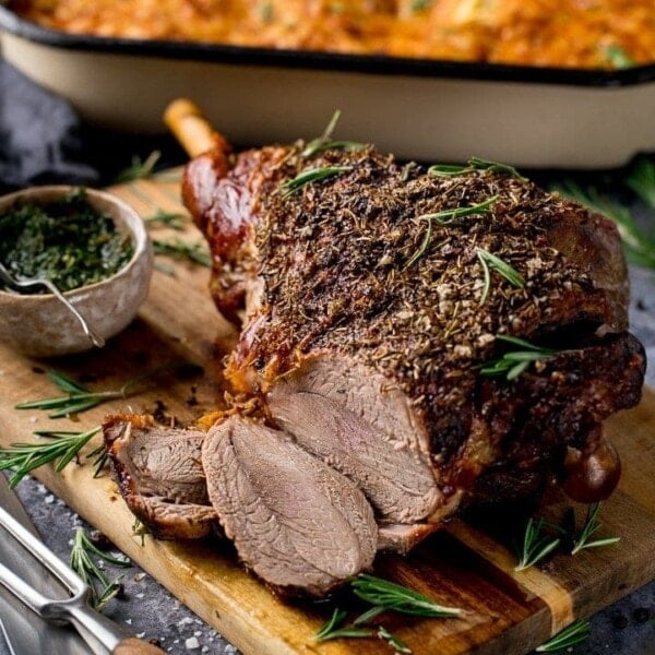 Sliced roast leg of lamb on a board with mint sauce