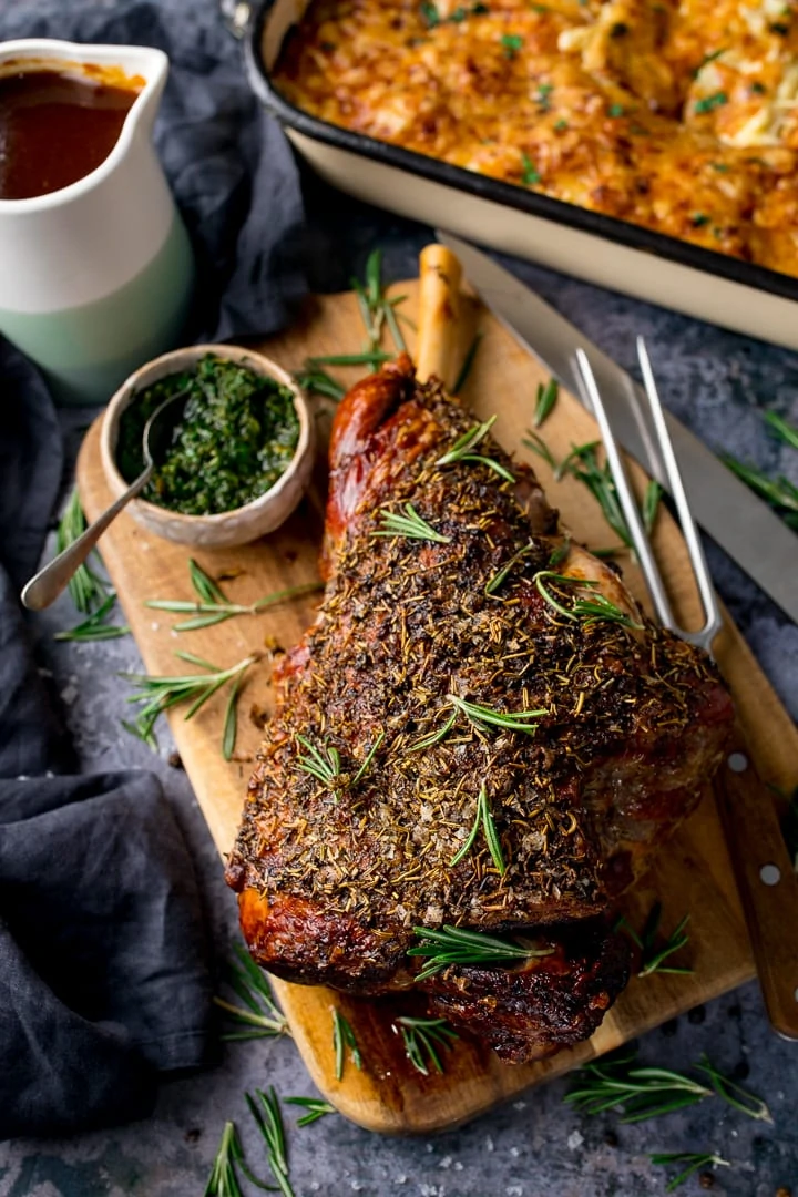 leg of lamb on a wooden board next to a pot of mint sauce