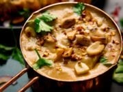 Satay sauce in a small copper pan topped with peanuts and coriander