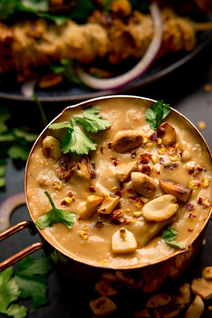 Peanut satay sauce in a small copper pan topped with peanuts and coriander