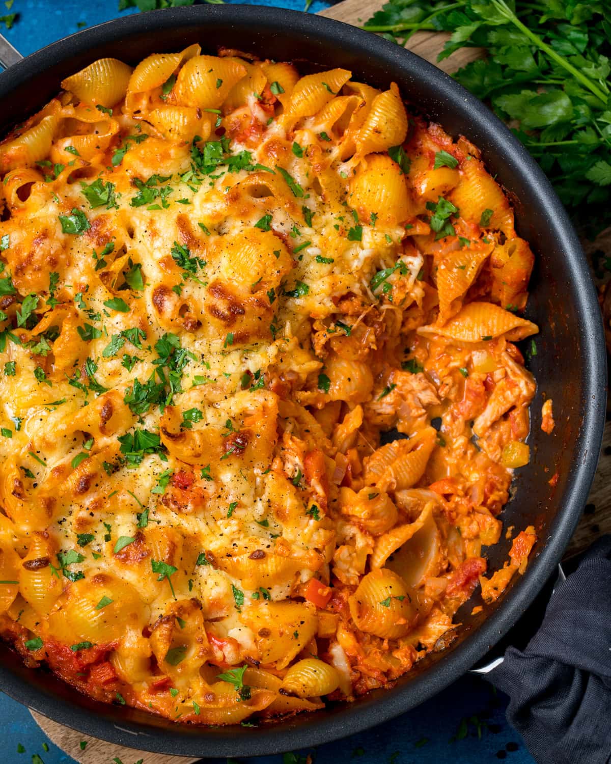 Tuna pasta bake with pasta shells in a frying pan, topped with melted cheese and chopped parsley, with a portion served out to reveal creamy tomato sauce.