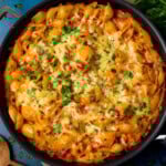 Overhead image of a creamy tuna tomato pasta bake topped with melted cheese and chopped parsley. The dish is on a blue surface.