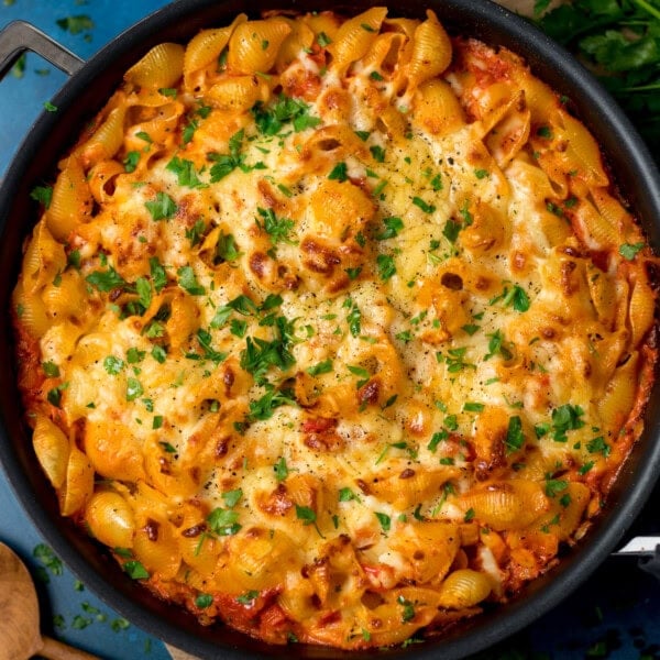 Overhead image of a creamy tuna tomato pasta bake topped with melted cheese and chopped parsley. The dish is on a blue surface.