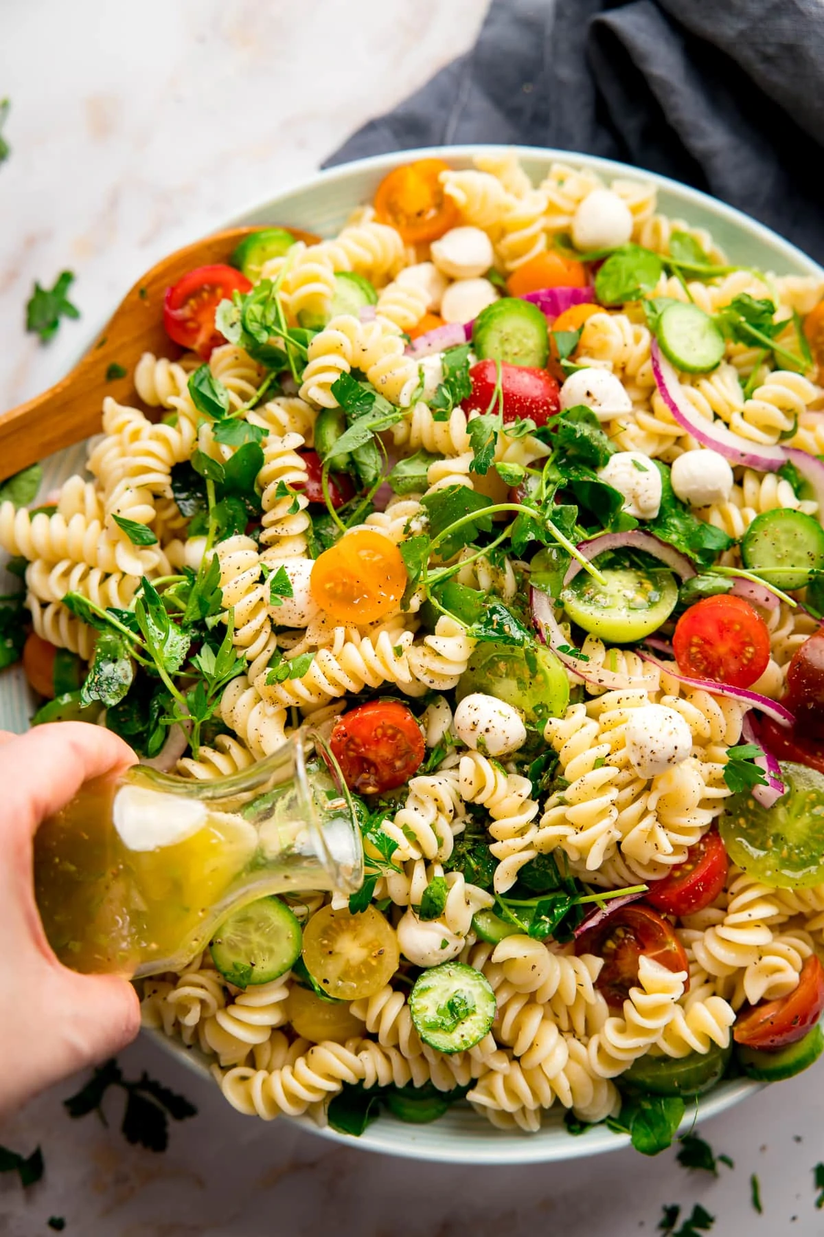 Italian dressing being poured onto a bowl of pasta salad