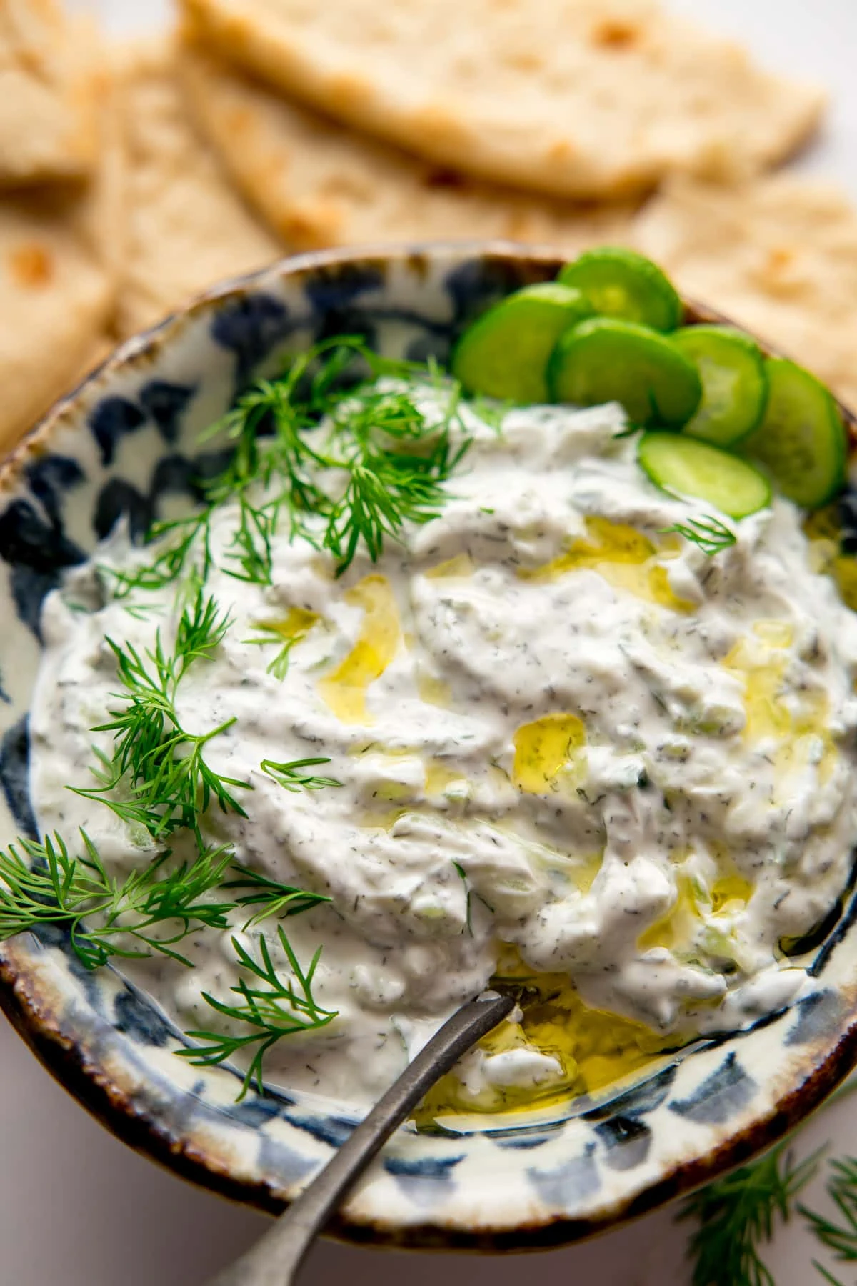A bowl of Tzatziki with flatbreads on a light background