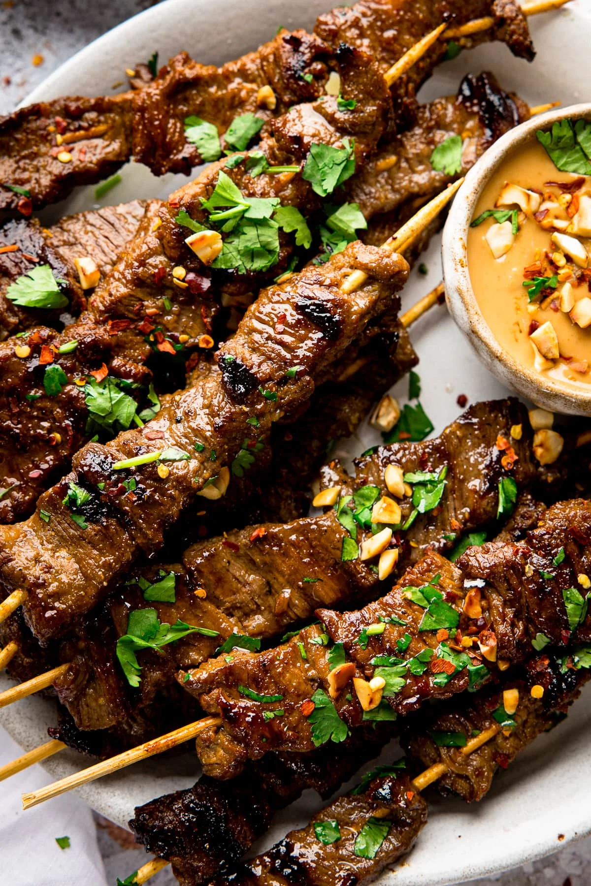 Close up of beef satay skewers on a plate, topped with coriander and peanuts