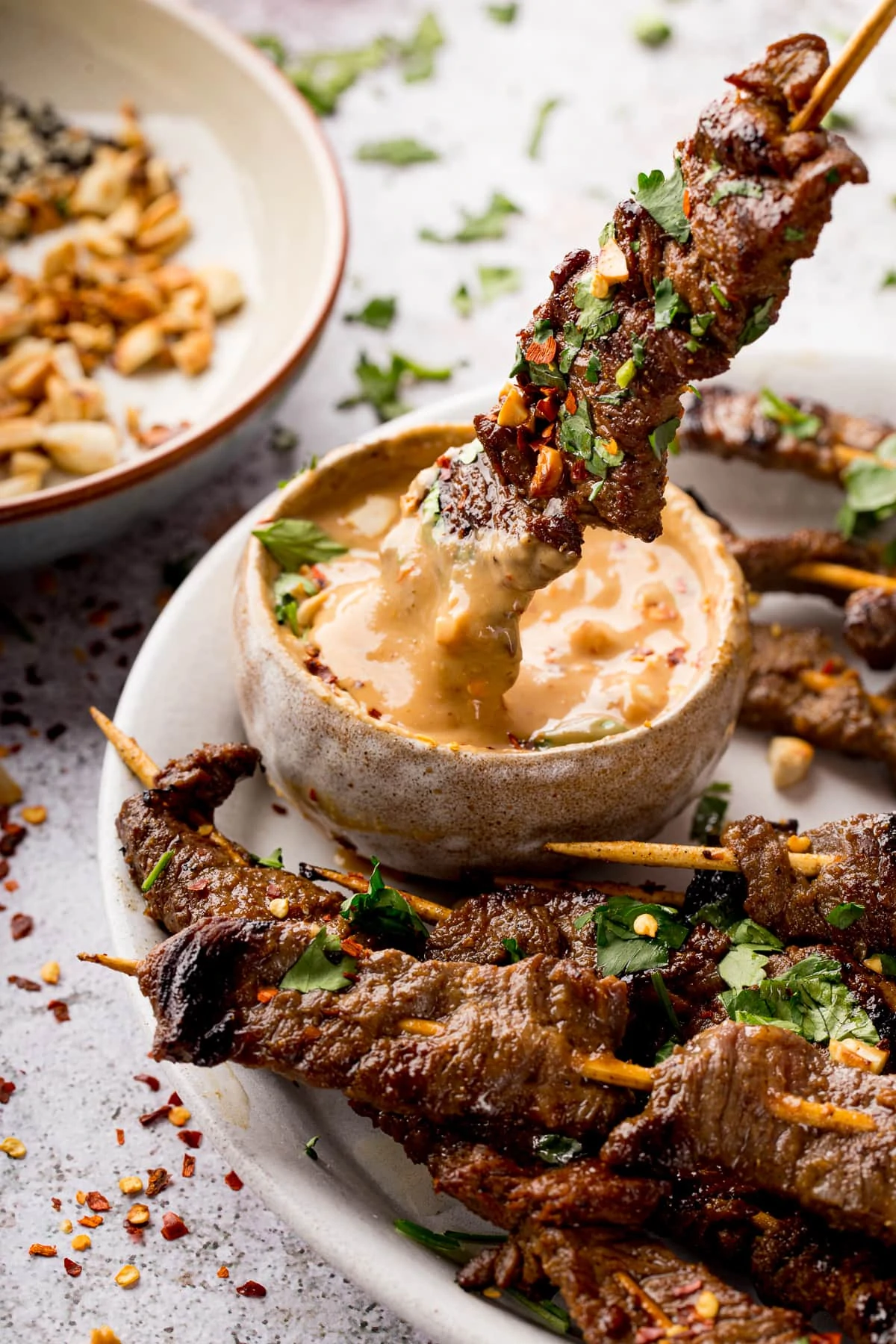 beef satay skewer being dipped into satay sauce.