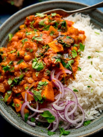 chickpea and sweet potato curry in a bowl with rice and red onion