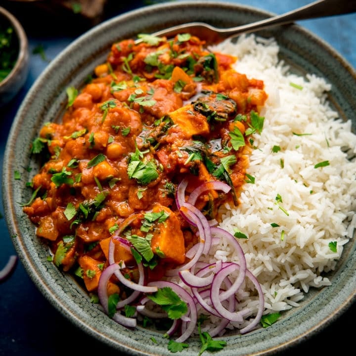 chickpea and sweet potato curry in a bowl with rice and red onion