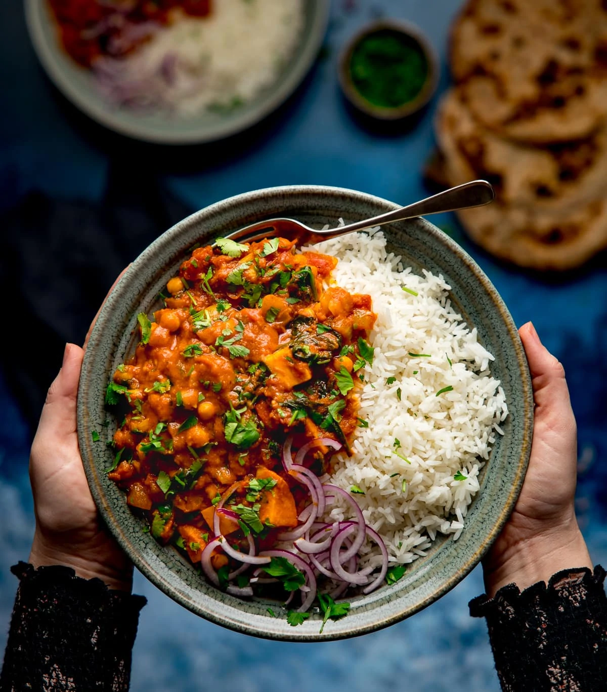 Bowl of chickpea and sweet potato curry with rice being held by two hands