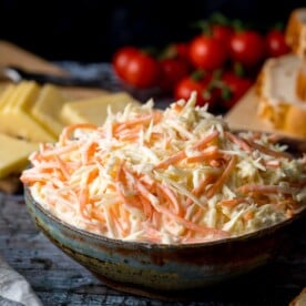 creamy coleslaw in a bowl. Cheese and cherry tomatoes in the background