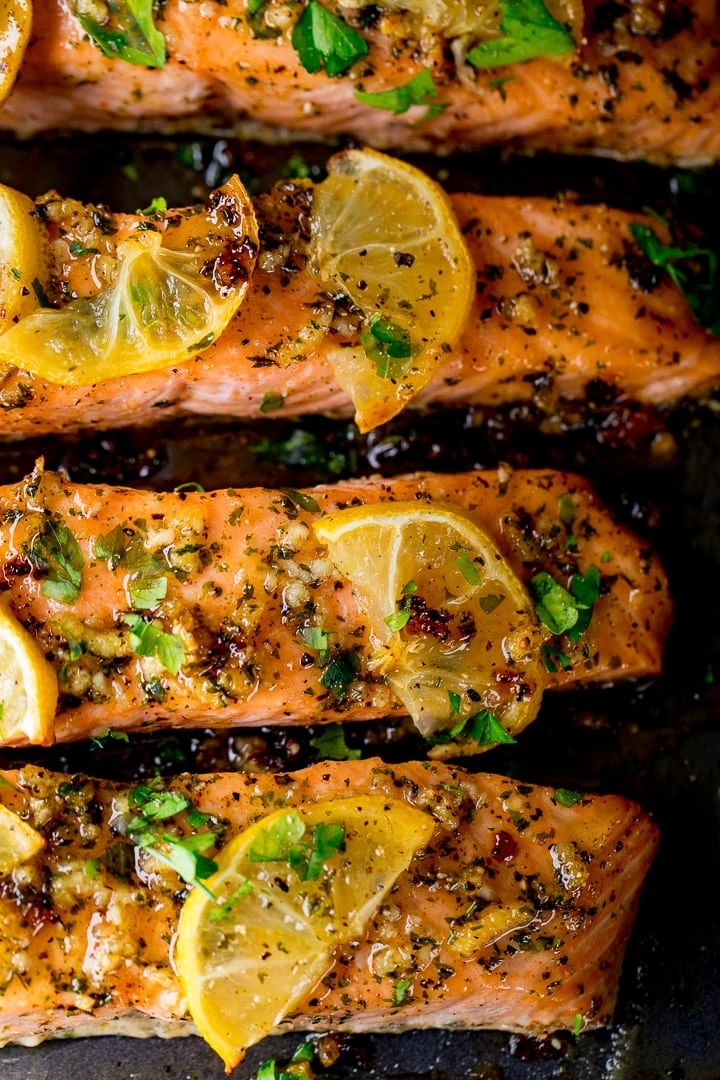 4 fillets of honey garlic baked salmon on a tray topped with lemon slices and herbs