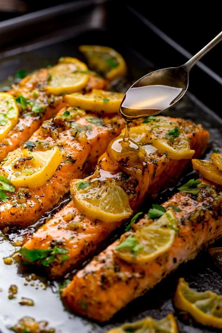 Spoonful of honey being poured onto honey garlic baked salmon on a baking tray.