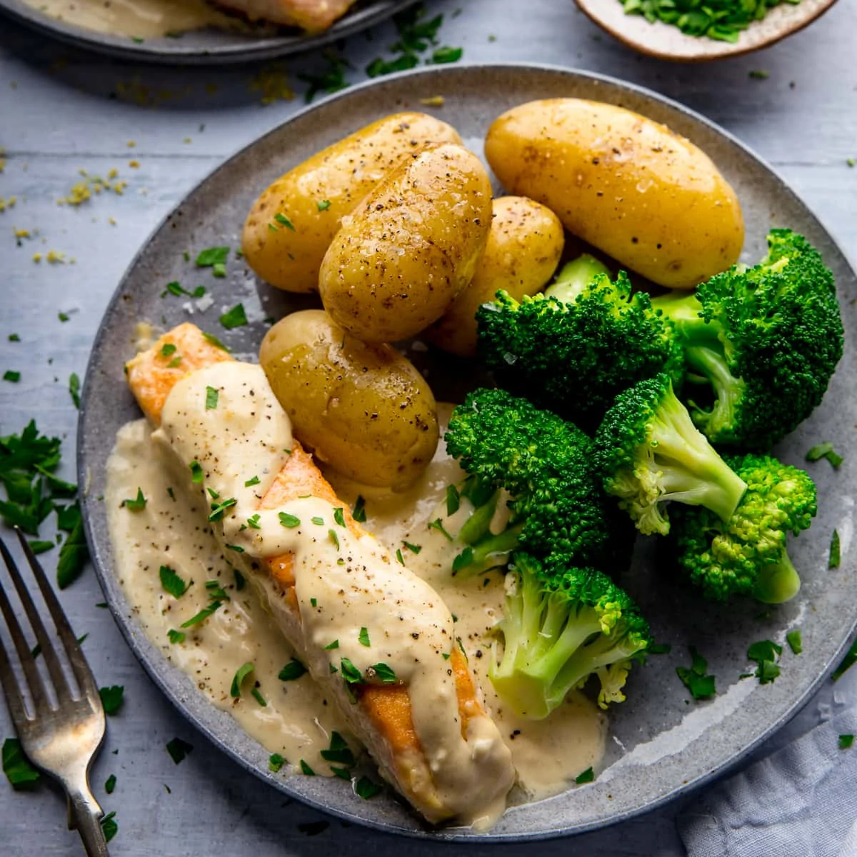 Salmon on a grey plate with creamy white wine sauce, broccoli and new potatoes