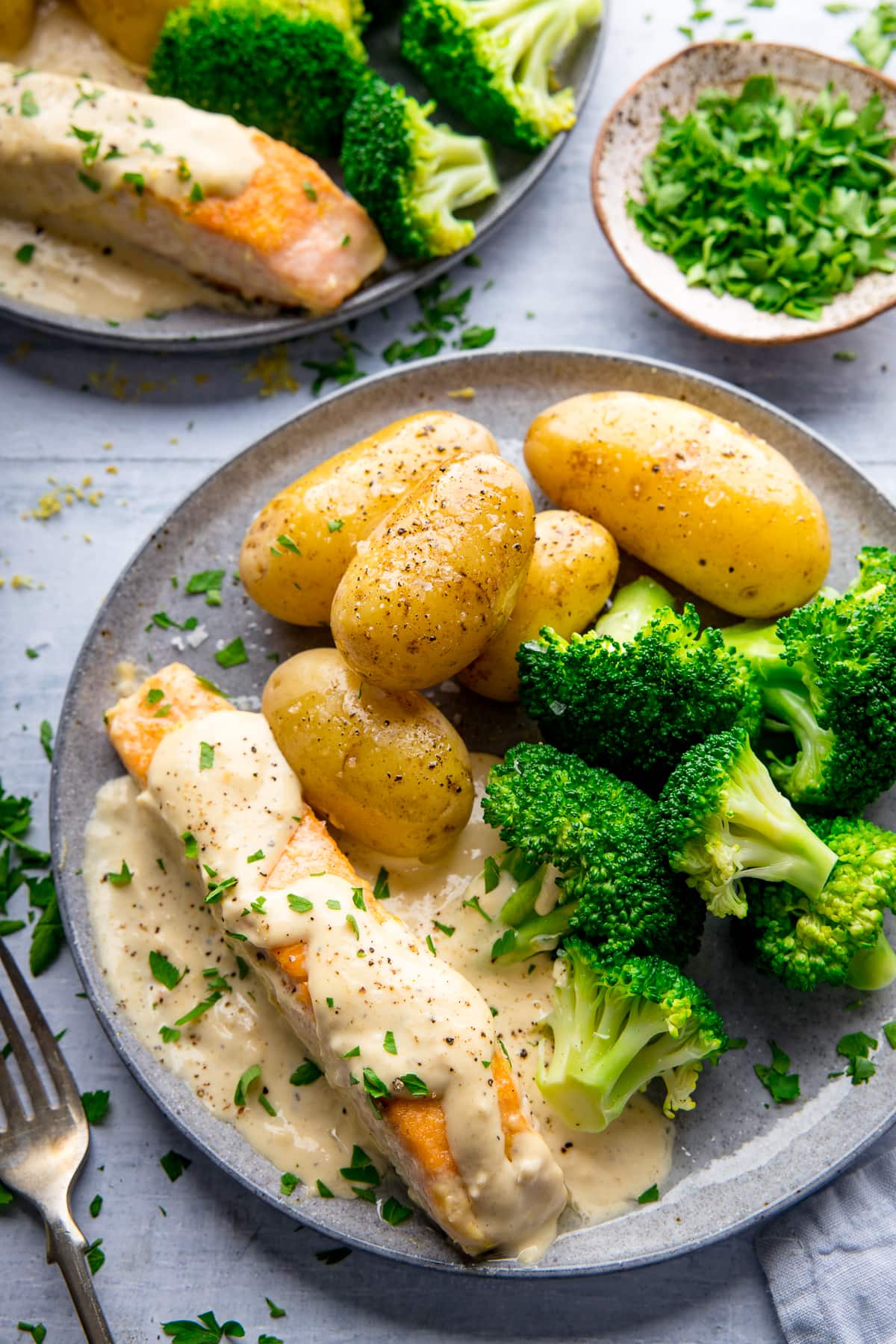 Grey plate with salmon drizzled in a creamy sauce served with broccoli and potatoes