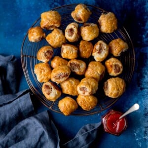 Square image of sausage rolls on a cooling rack on a dark blue background