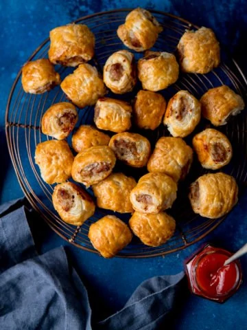 Square image of sausage rolls on a cooling rack on a dark blue background