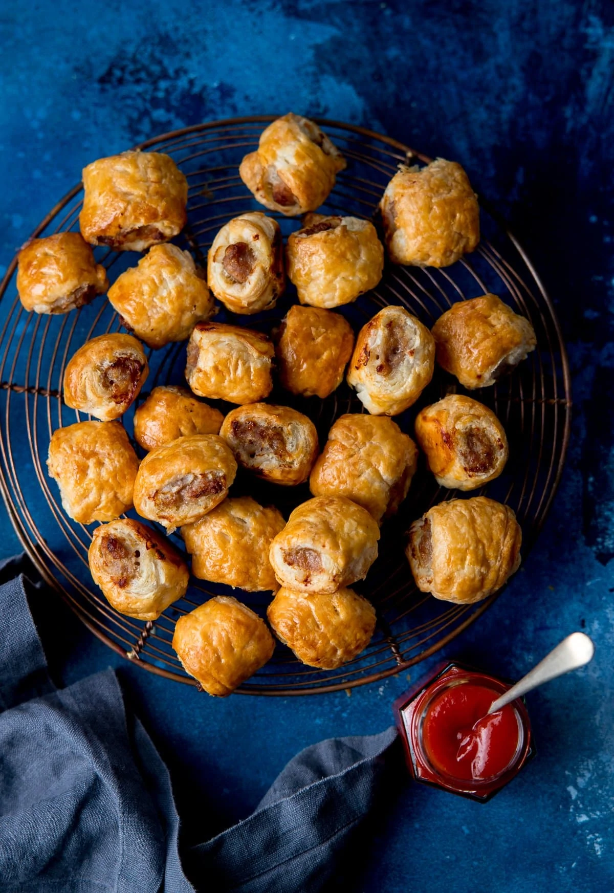 sausage rolls on a cooling rack on a dark blue background with a pot of ketchup