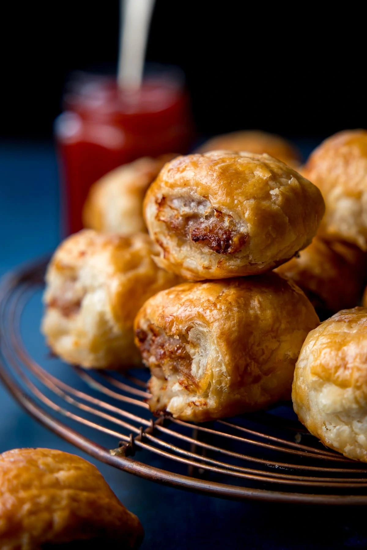 close up of two sausage rolls on a cooling rack. Pot of ketchup in the background