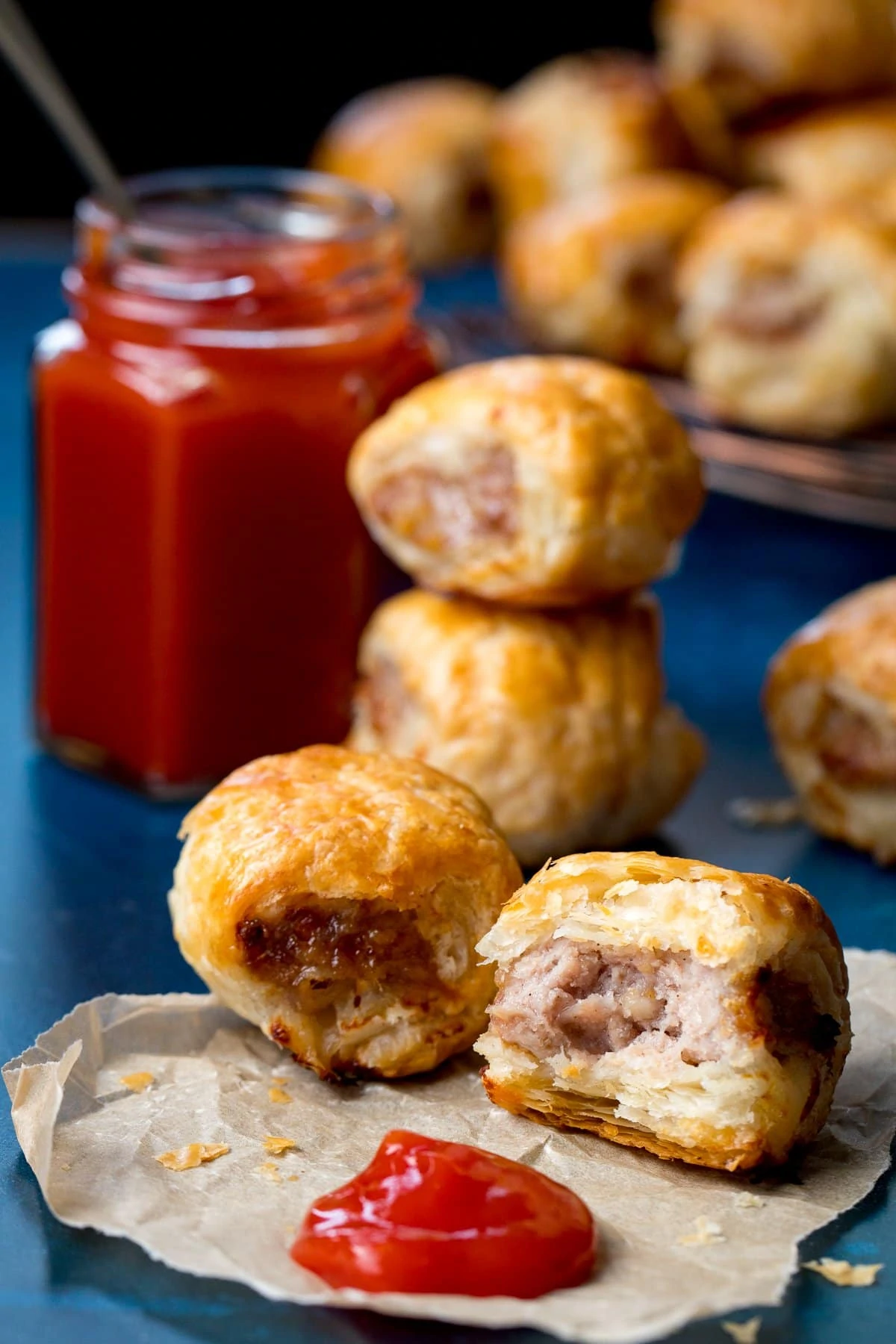 Sausage rolls and a blob of ketchup on a piece of parchment. Bite taken out of one of the sausage rolls.