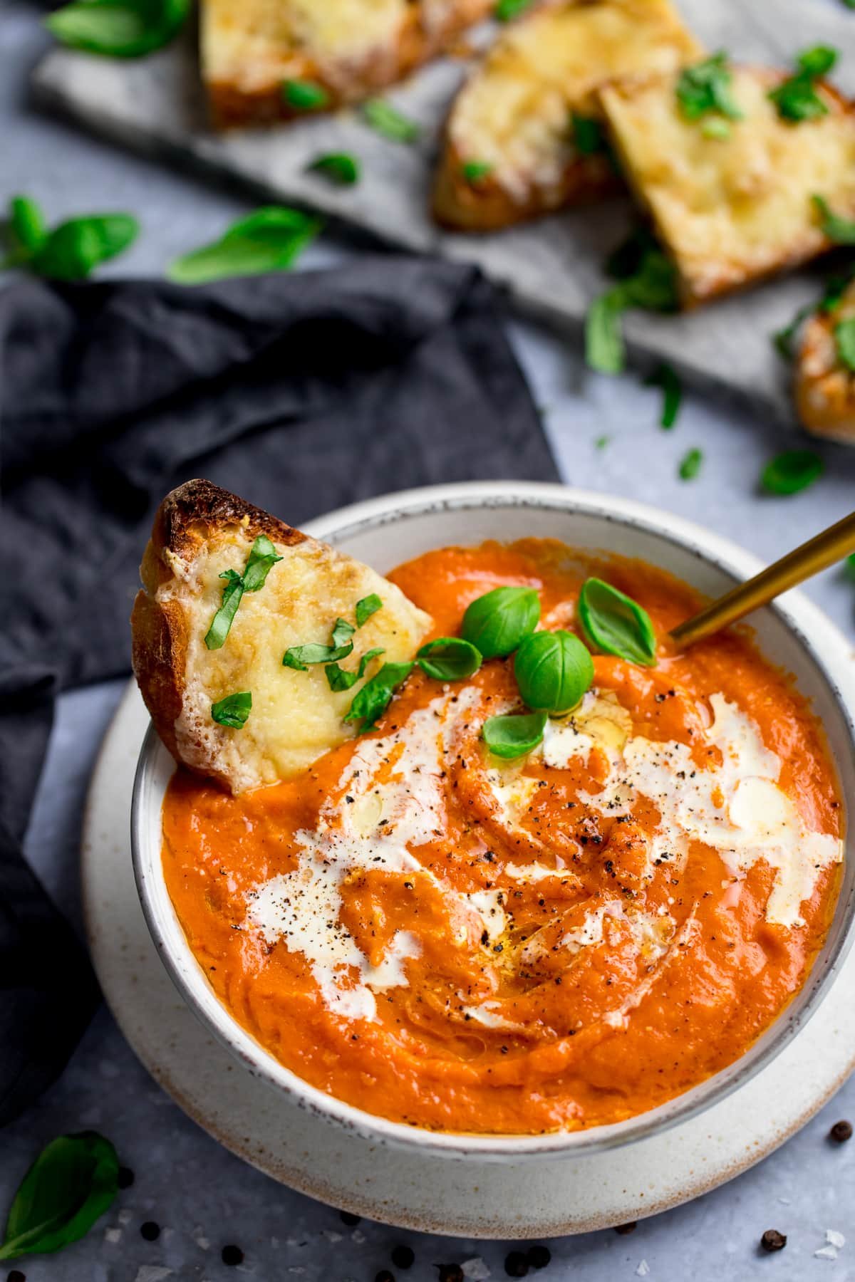 Bowl of rich tomato soup with a slice of basil-cheese toast in it, and more slices of cheese toast on the side.