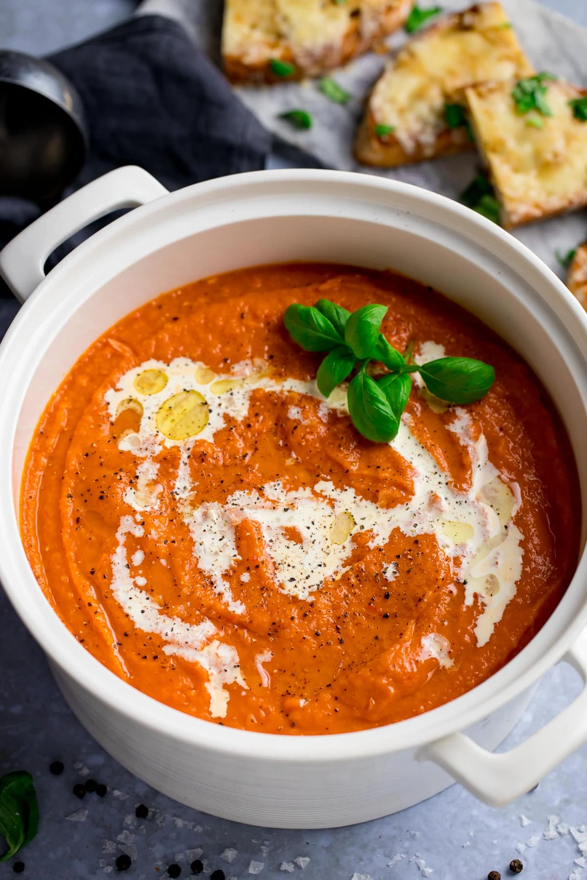 A pot of delicious tomato soup topped with double cream; and a plate of cheese toast on the side.