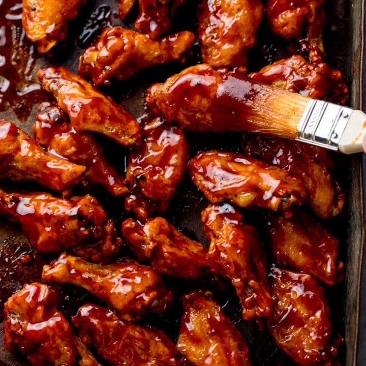 BBQ chicken wings on a tray with BBQ sauce being brushed on